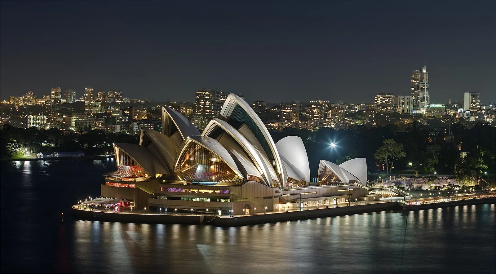 Opera House de Sydney iluminada junto ao porto durante a noite.